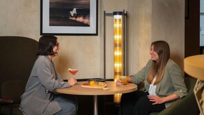 Two people seated at a round table with drinks, a framed picture on the wall, and a tall, illuminated column in the background. - Hotel Maison Louise Lille Centre - Handwritten Collection (Lille)