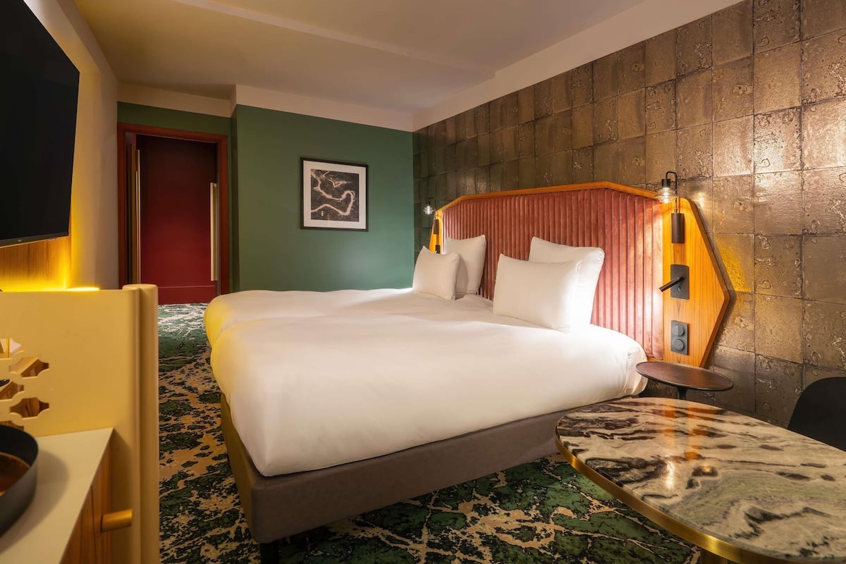 Une chambre d’hôtel équipée d’un lit, d’un bureau, d’une chaise, d’une table et d’une lampe fixée au mur.