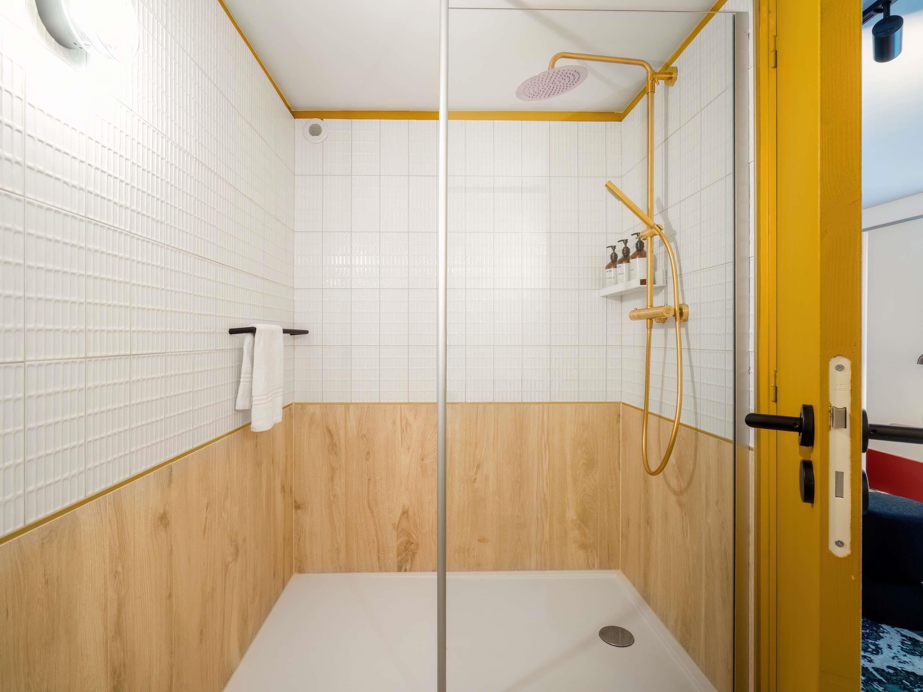 A shower with a glass door, white tiled walls, and a wooden lower section.