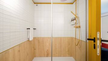 A shower with a glass door, white tiled walls, and a wooden lower section.