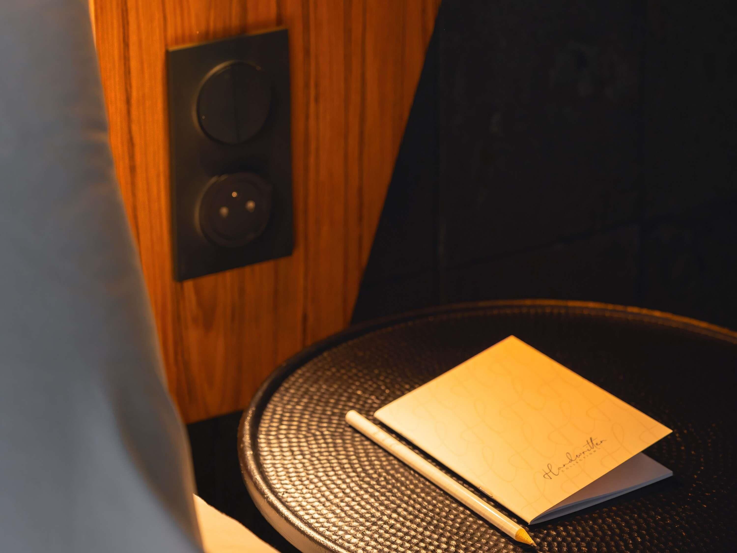 A notebook on a round table with a textured surface, a pen beside it, and a speaker on the wall.