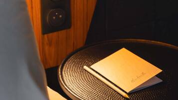 A notebook on a round table with a textured surface, a pen beside it, and a speaker on the wall.