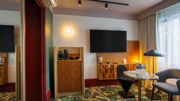 Une chambre d’hôtel dotée d’un grand téléviseur à écran plat, d’une petite kitchenette, d’une table ronde avec des chaises et d’un tapis à motifs.