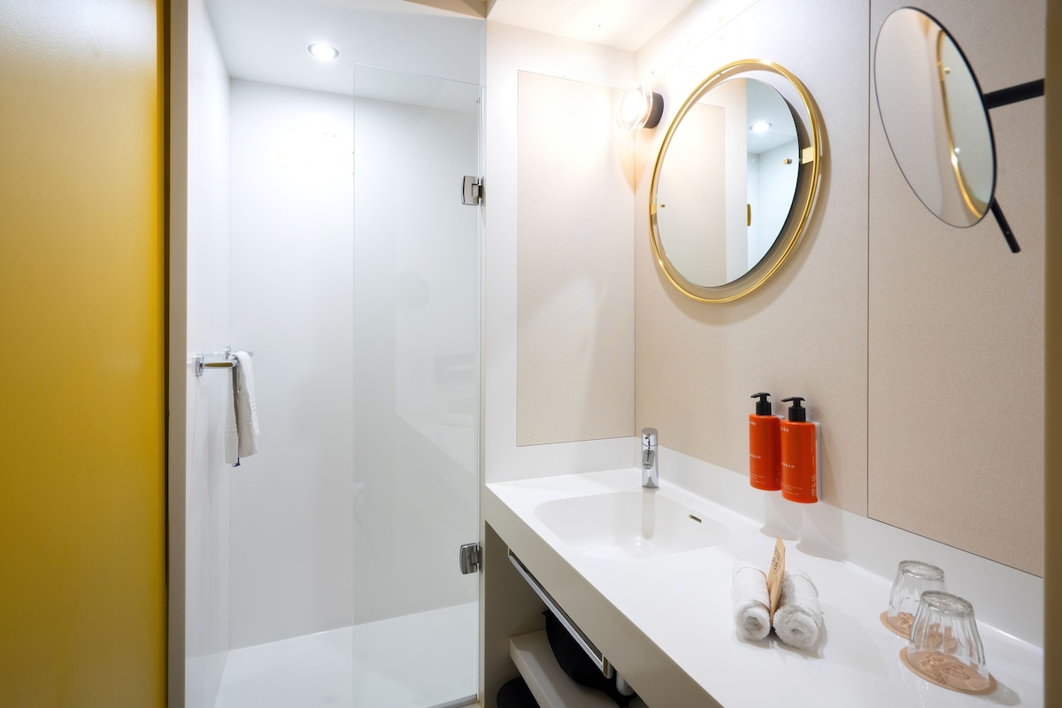 Un baño moderno con cabina de ducha de vidrio, un lavabo blanco y dos espejos redondos.