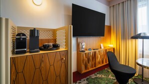 Een moderne hotelkamer met een houten kast, een koffieapparaat, een flatscreen televisie en een comfortabele fauteuil.