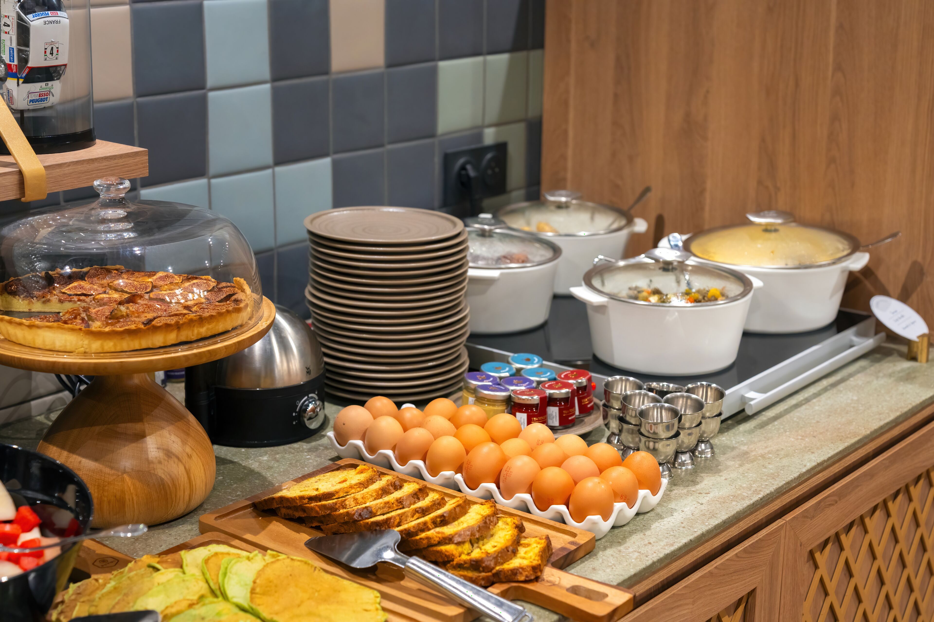Une table de buffet proposant divers plats, notamment une quiche, des œufs et du pain.