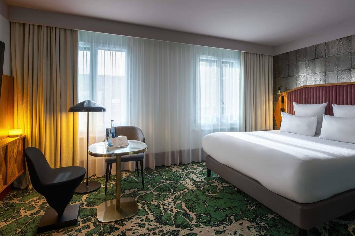 Een hotelkamer met een bed, een ronde tafel met een stoel, een lamp en gordijnen.