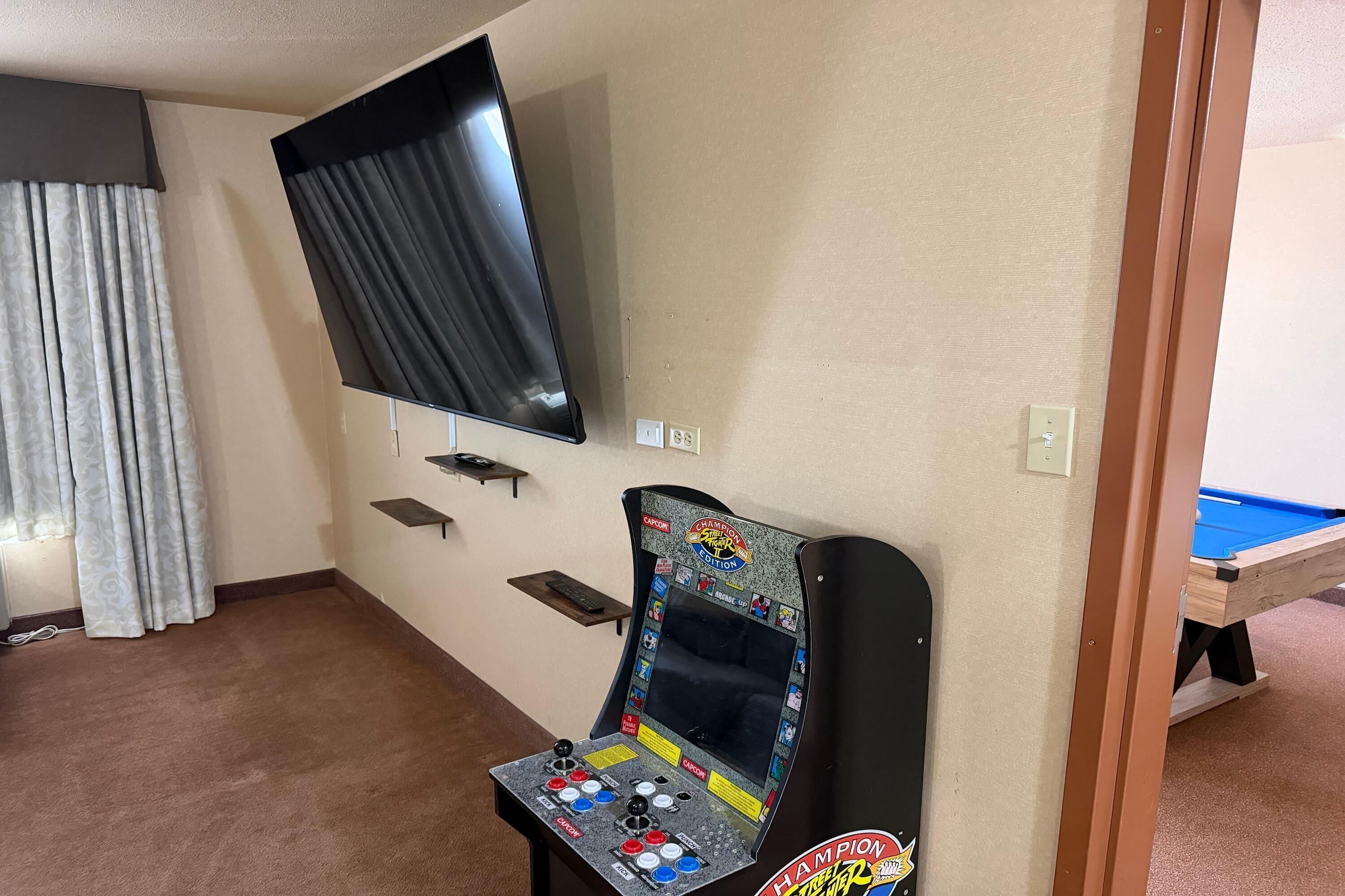 Una habitación con mesa de billar, televisor montado en la pared y mesa de billar con panel de control colorido.