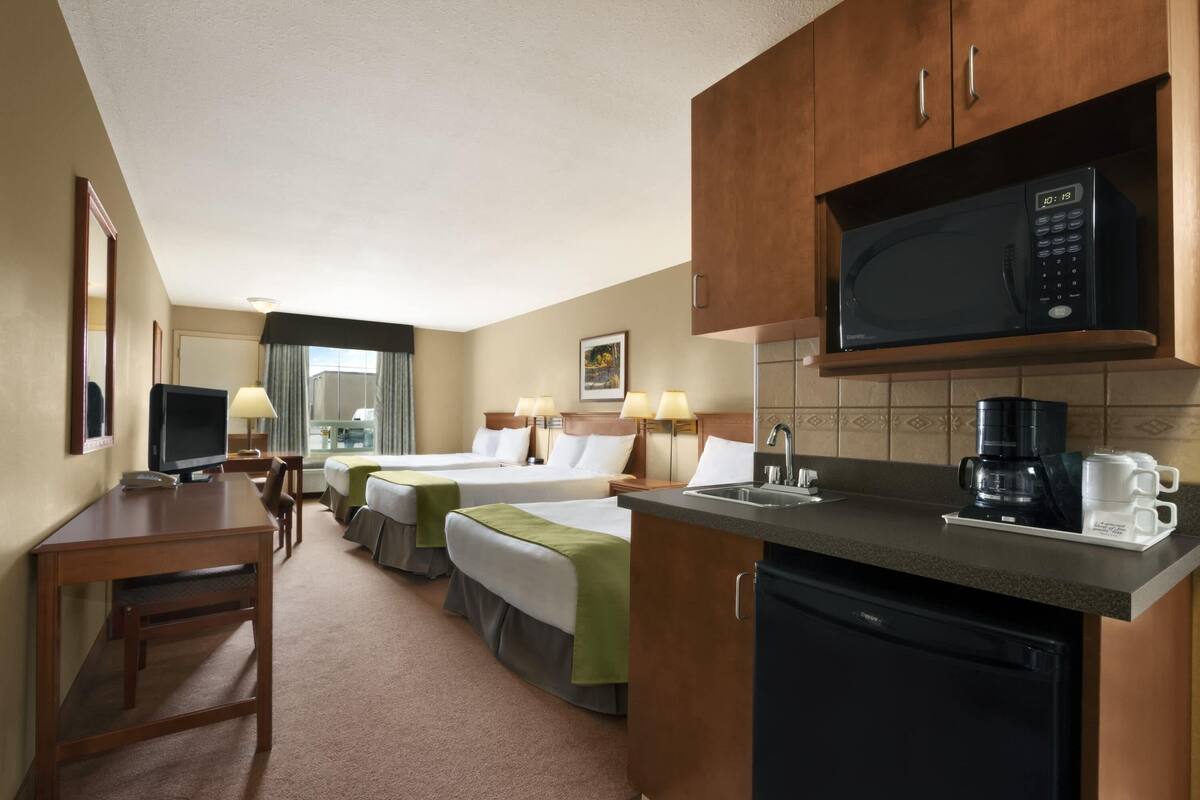 Une chambre d’hôtel avec deux lits, un bureau, une télévision, un four à micro-ondes, une machine à café et un lavabo.