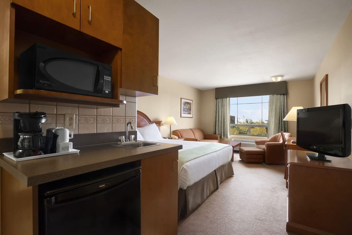 Une chambre d’hôtel équipée d’une kitchenette, d’un lit, d’une télévision et d’une fenêtre donnant sur un paysage agréable.