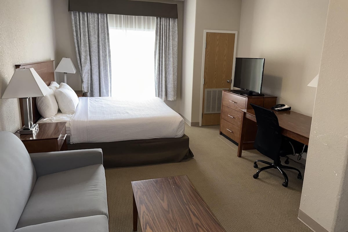 Une chambre d’hôtel avec un lit, un bureau, une chaise, une télévision et une lampe.