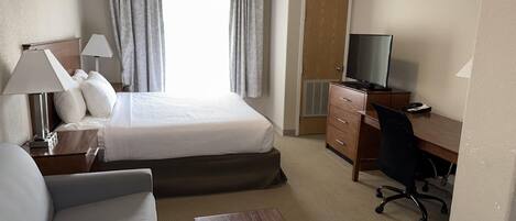 Hotellihuone, jossa on sänky, työpöytä, tuoli, televisio ja lamppu.