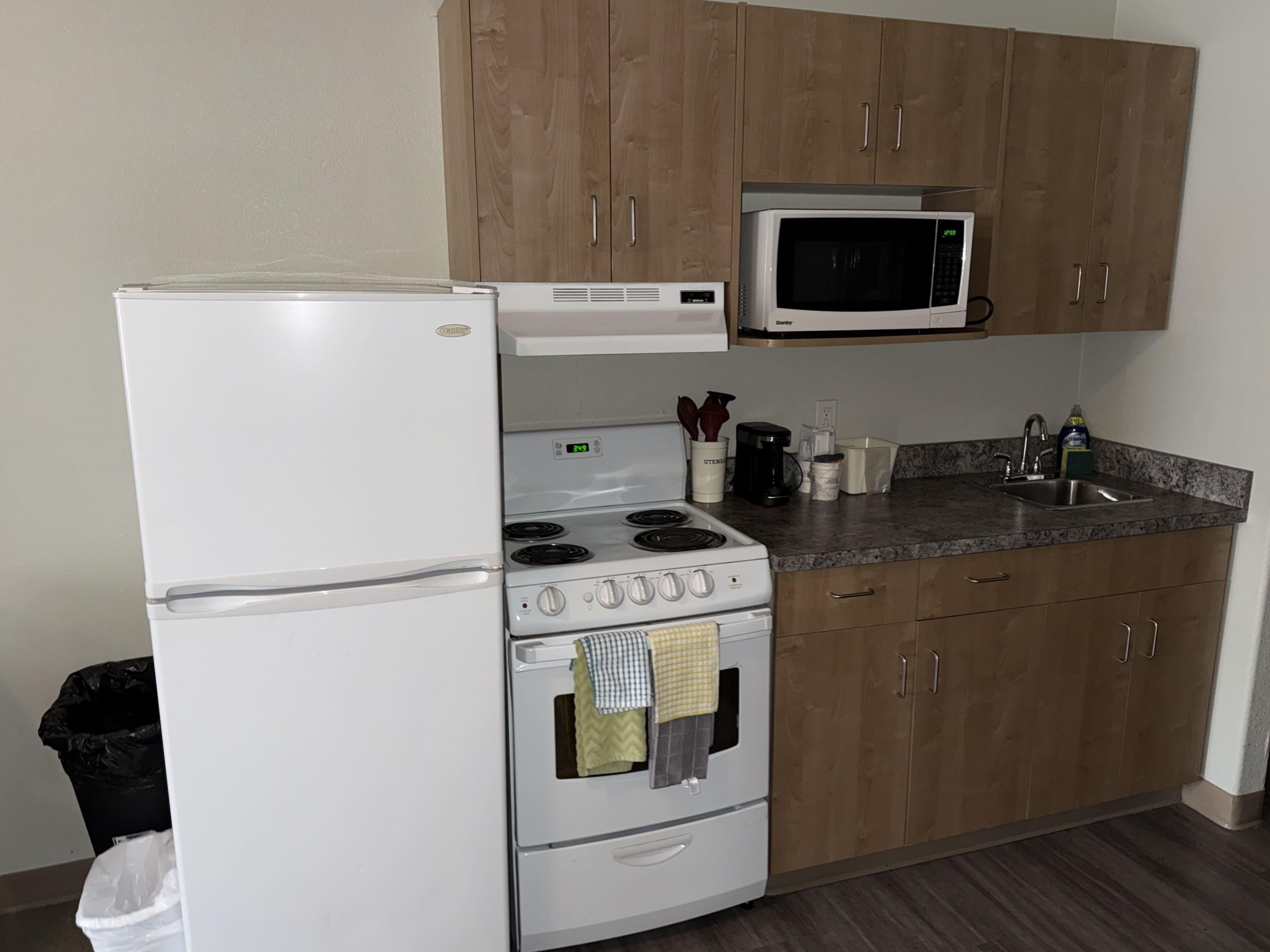 Cocina compacta con refrigerador, estufa, microondas y armarios de madera.