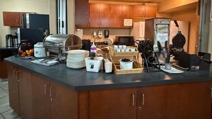 Estación de desayuno autoservicio con cafetera, máquina para hacer gofres y diferentes recipientes de comida.