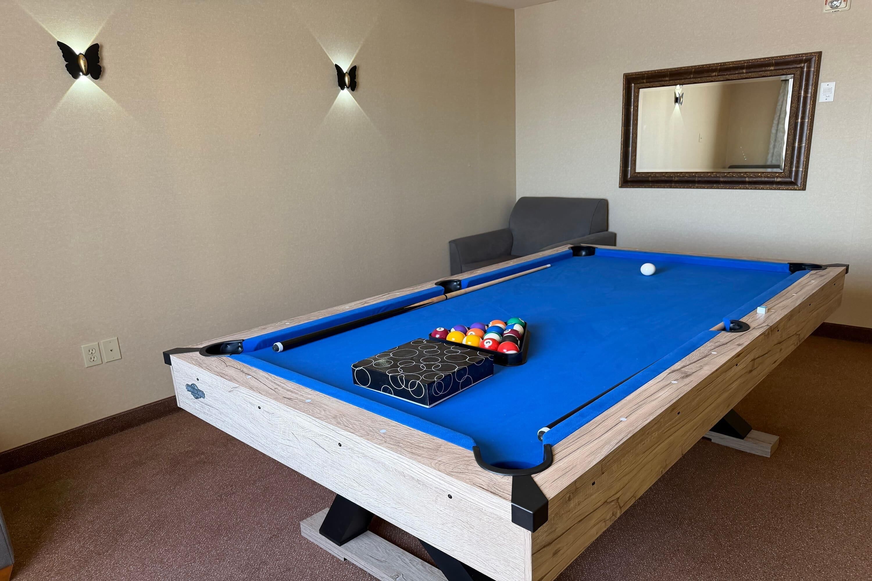 A pool table with a blue felt surface, surrounded by a light-colored carpet.