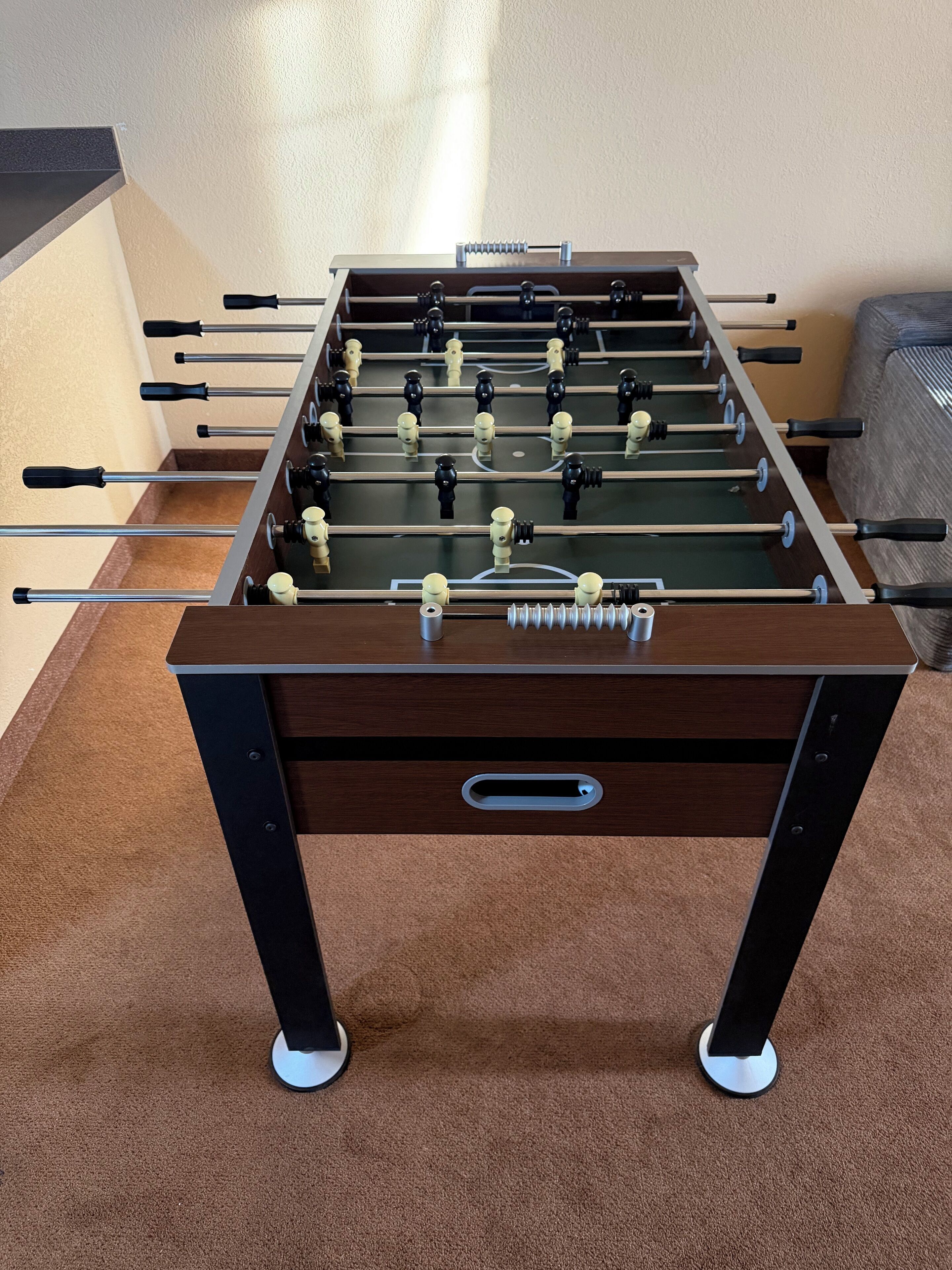 A foosball table with a drawer underneath, set on a carpeted floor.