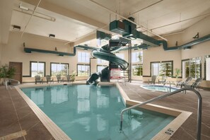 An indoor swimming pool with a water slide, lounge chairs, and a hot tub.