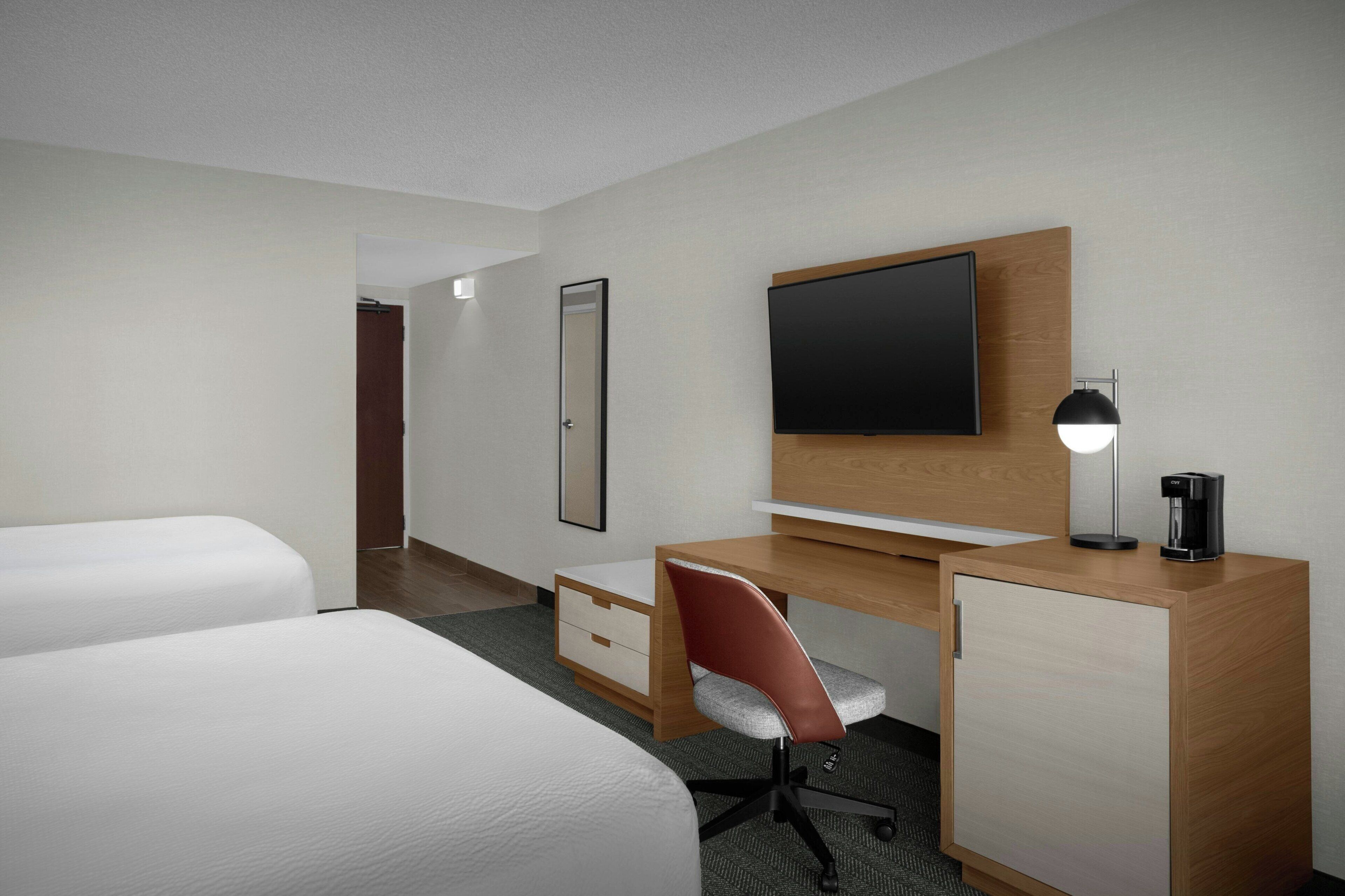 A hotel room with two beds, a desk with a chair, a television, a coffee maker, and a cabinet.