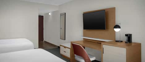 A hotel room with two beds, a desk with a chair, a television, a coffee maker, and a cabinet.