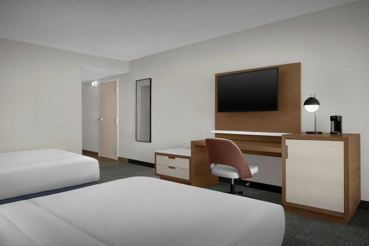 A hotel room with a bed, a desk with a chair, a television, a mirror, and a cabinet.