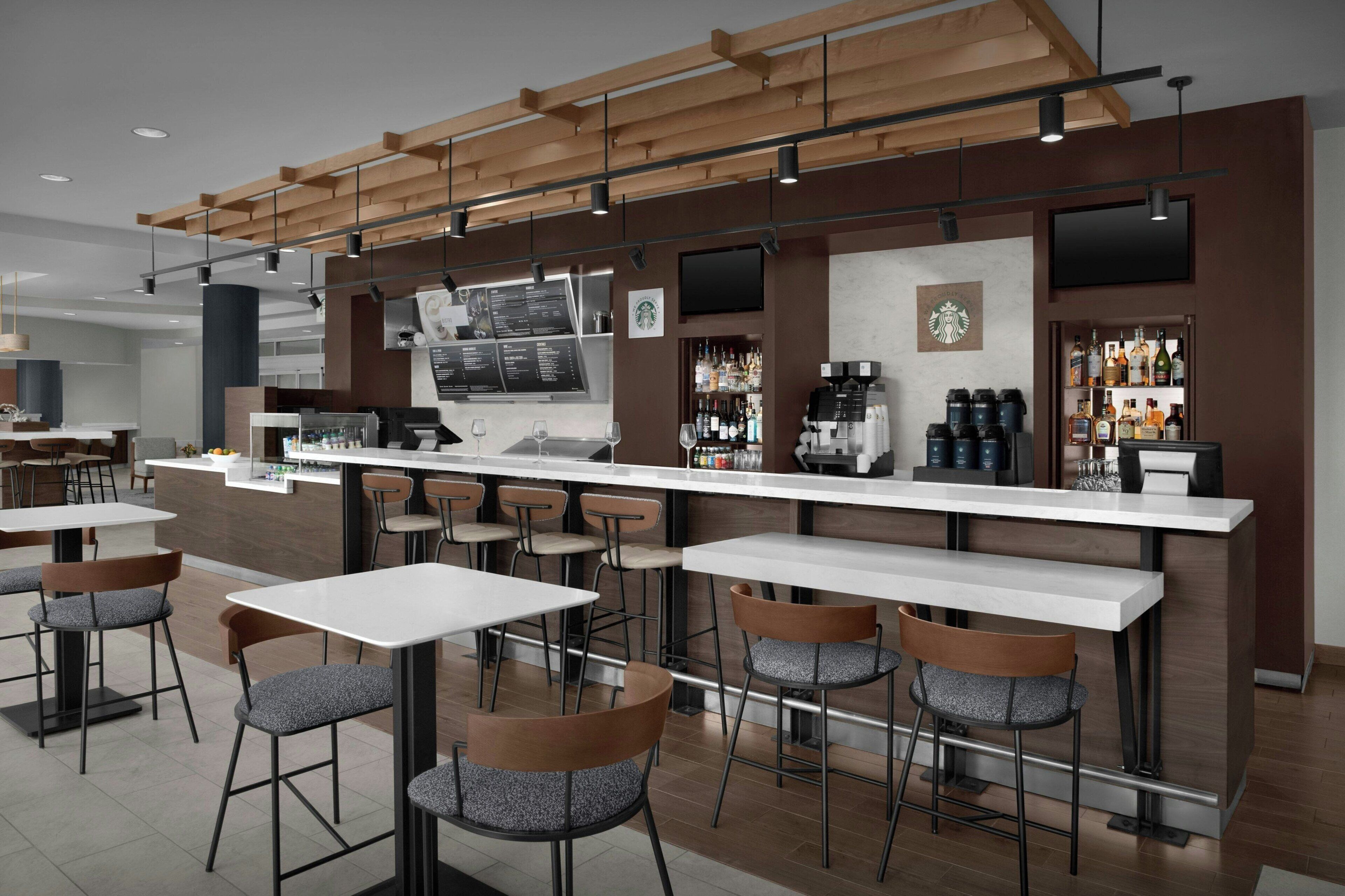 A modern bar area with a long counter, multiple stools, and a coffee machine.