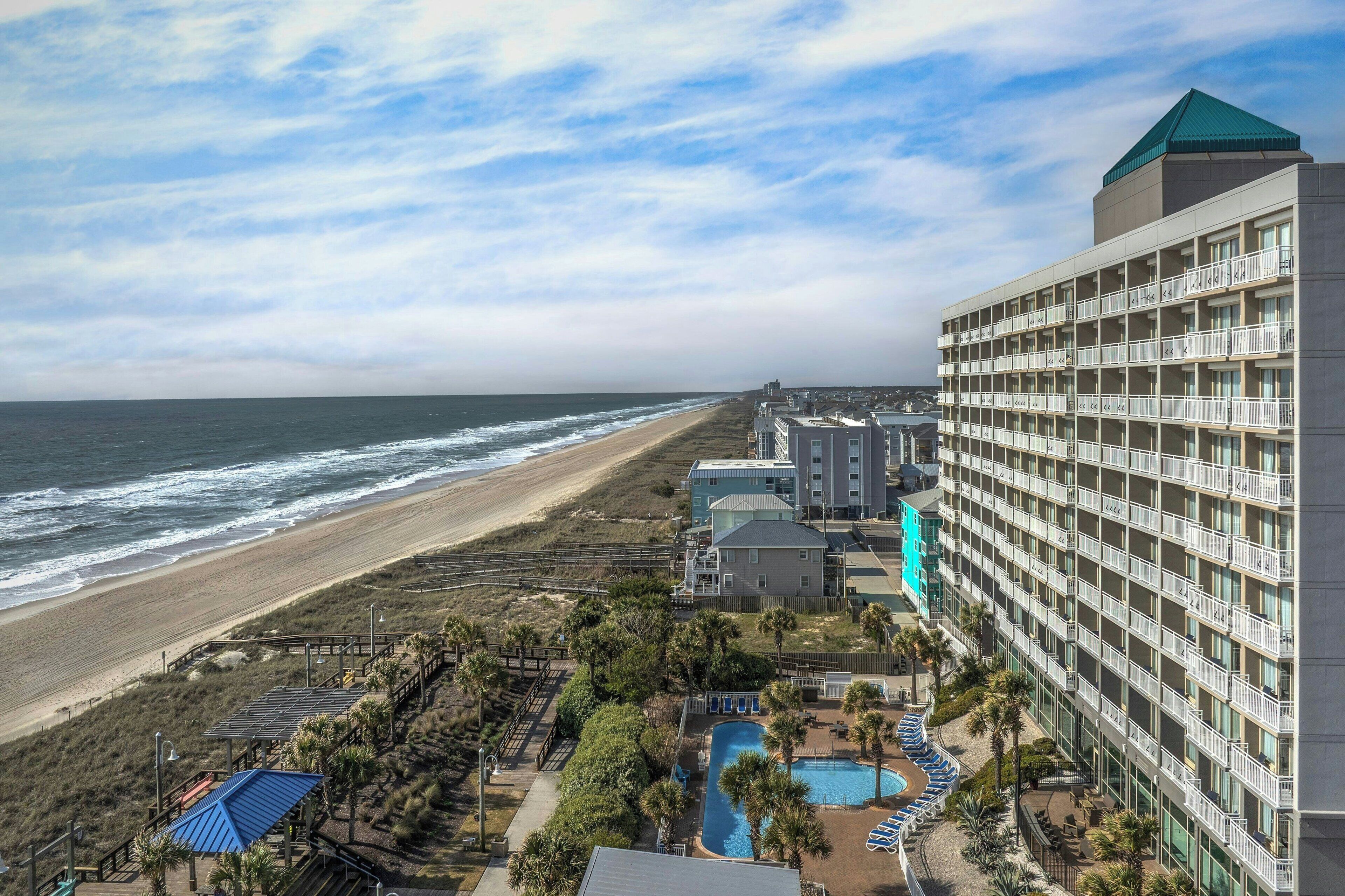 Un hotel frente a la playa con varios balcones, piscina y vista al mar.