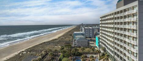 A beachfront hotel with multiple balconies, a swimming pool, and a beach view.
