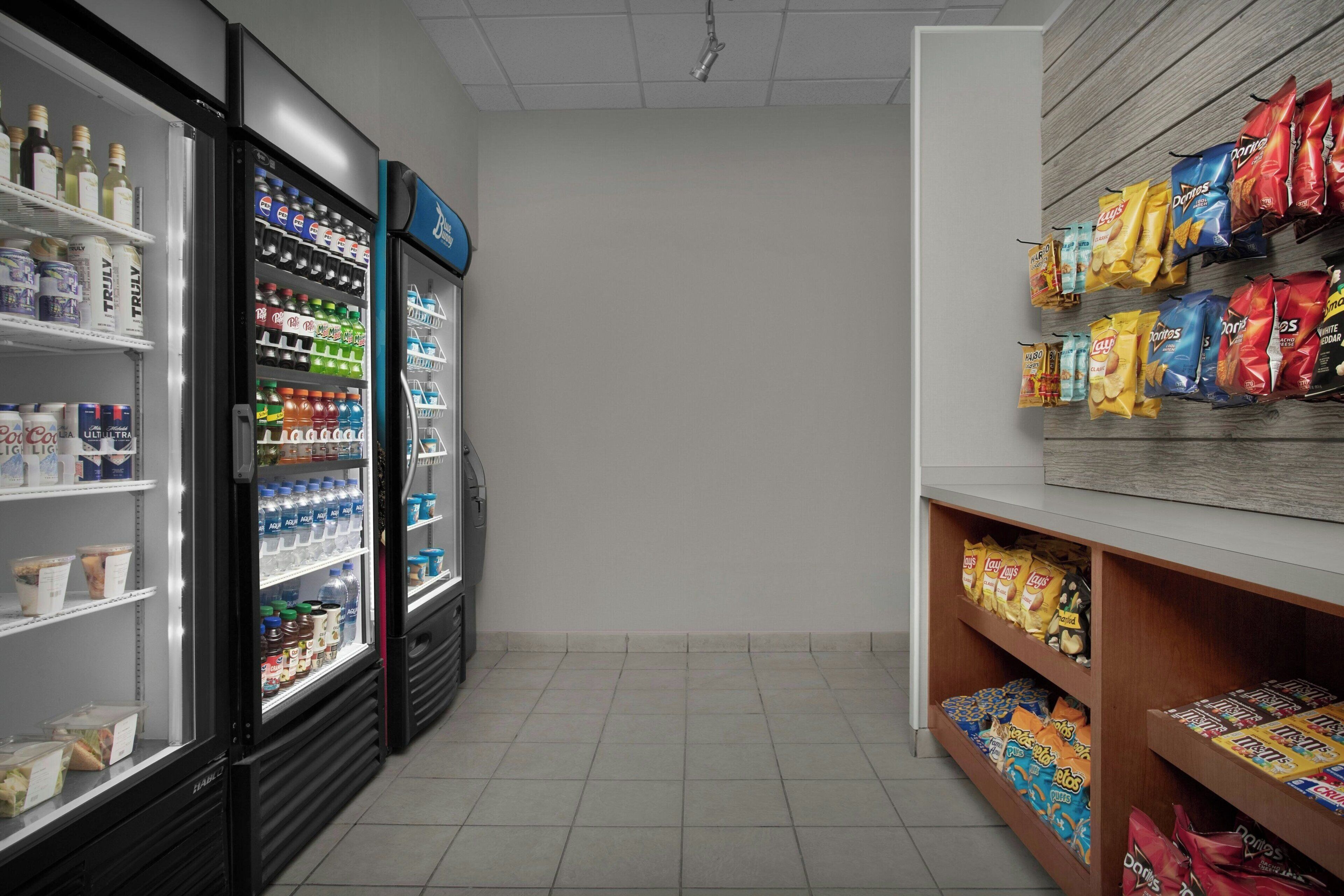 A clean, well-lit corridor with a refrigerated beverage display, snack shelves, and a plain wall.