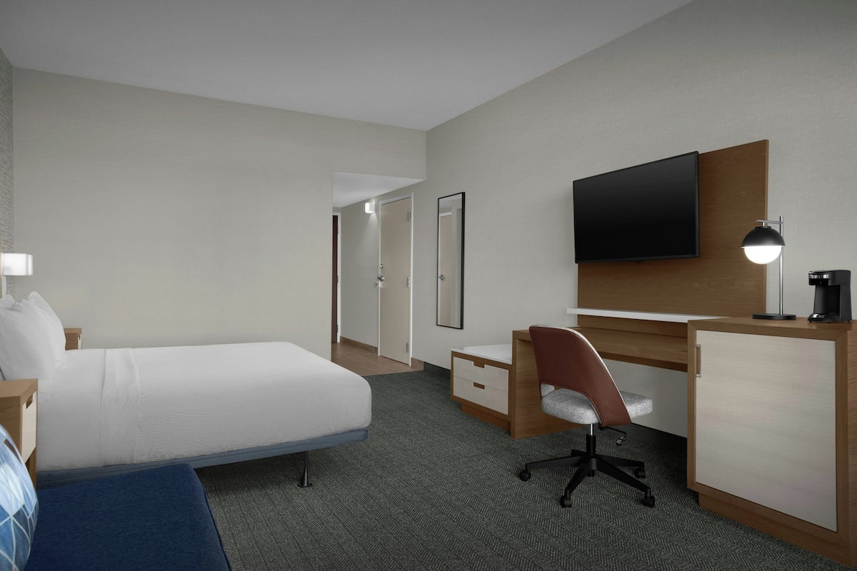 A hotel room with a bed, desk, chair, television, and a coffee maker.