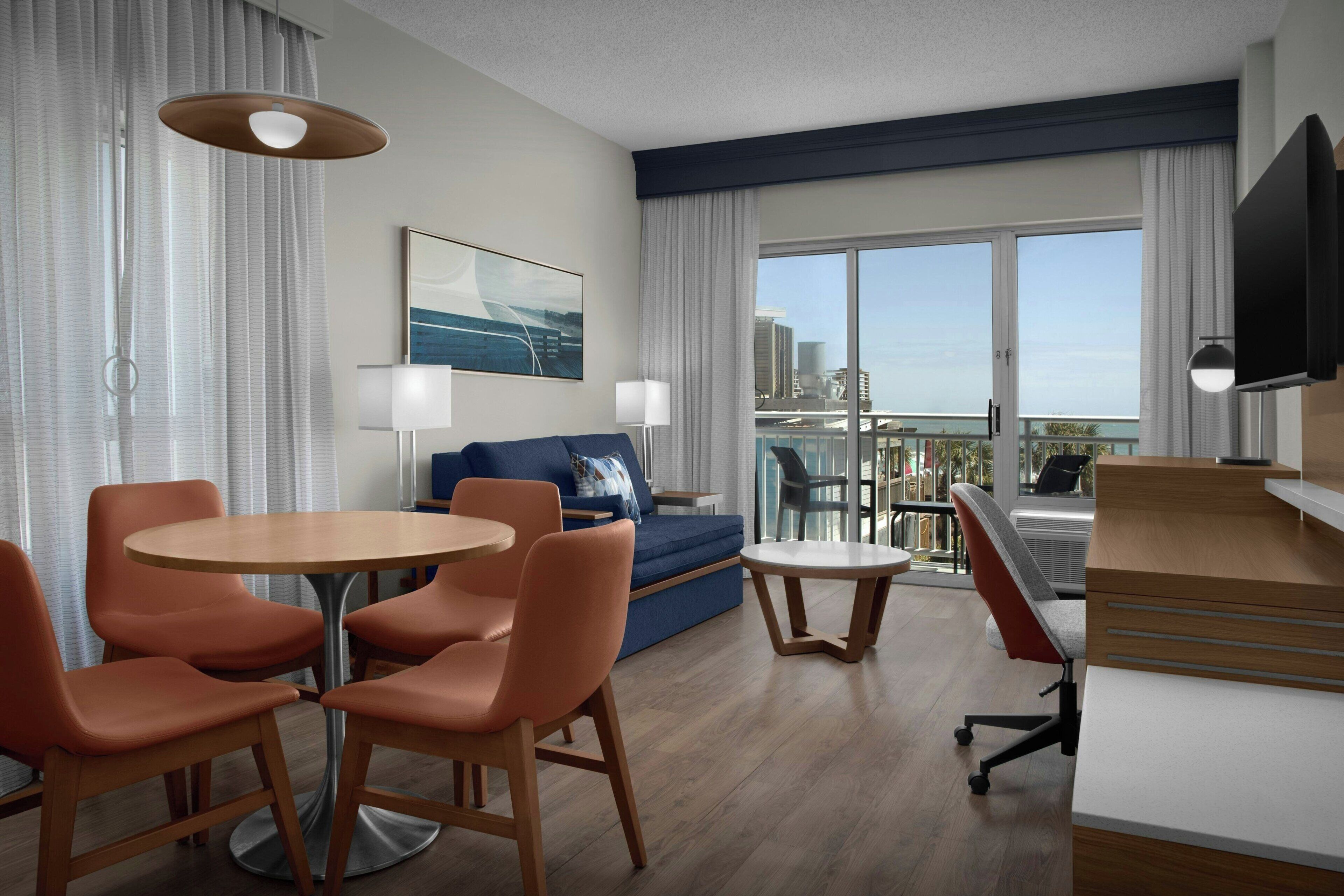 Ein Hotelzimmer mit Essbereich, einer Couch, einem Fernseher und einem Balkon mit Blick.