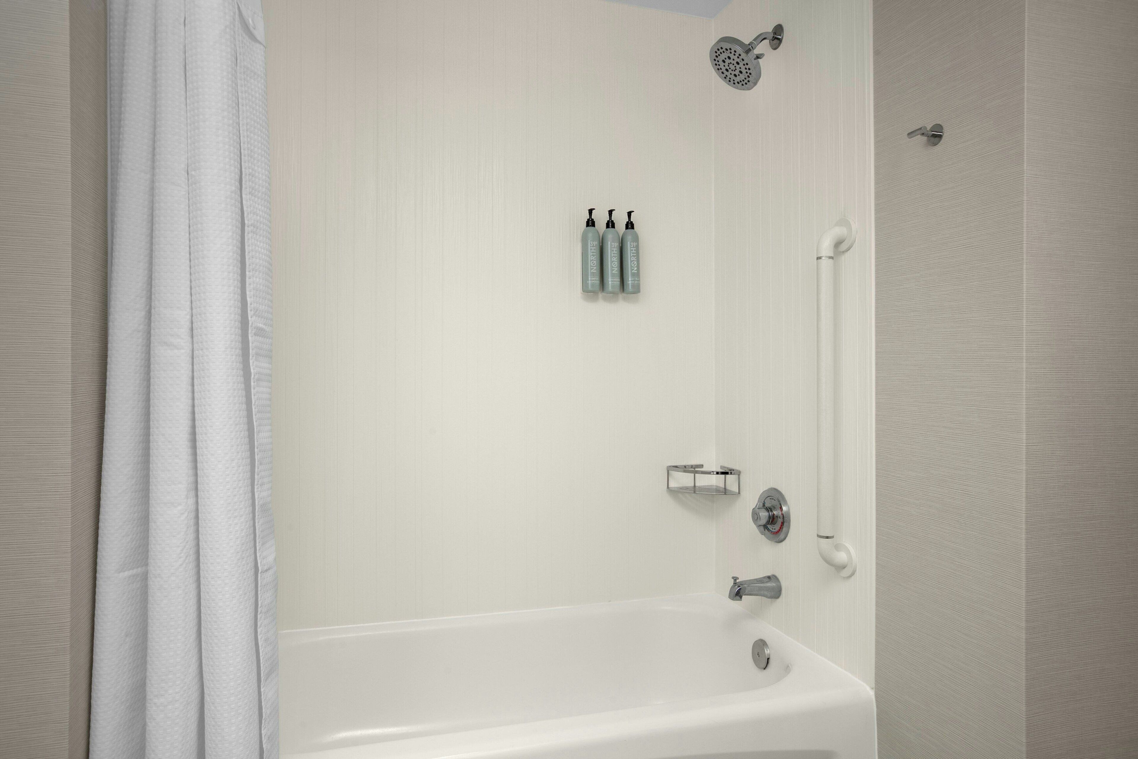 Un baño con bañera, ducha y dos botellas de champú en la pared.