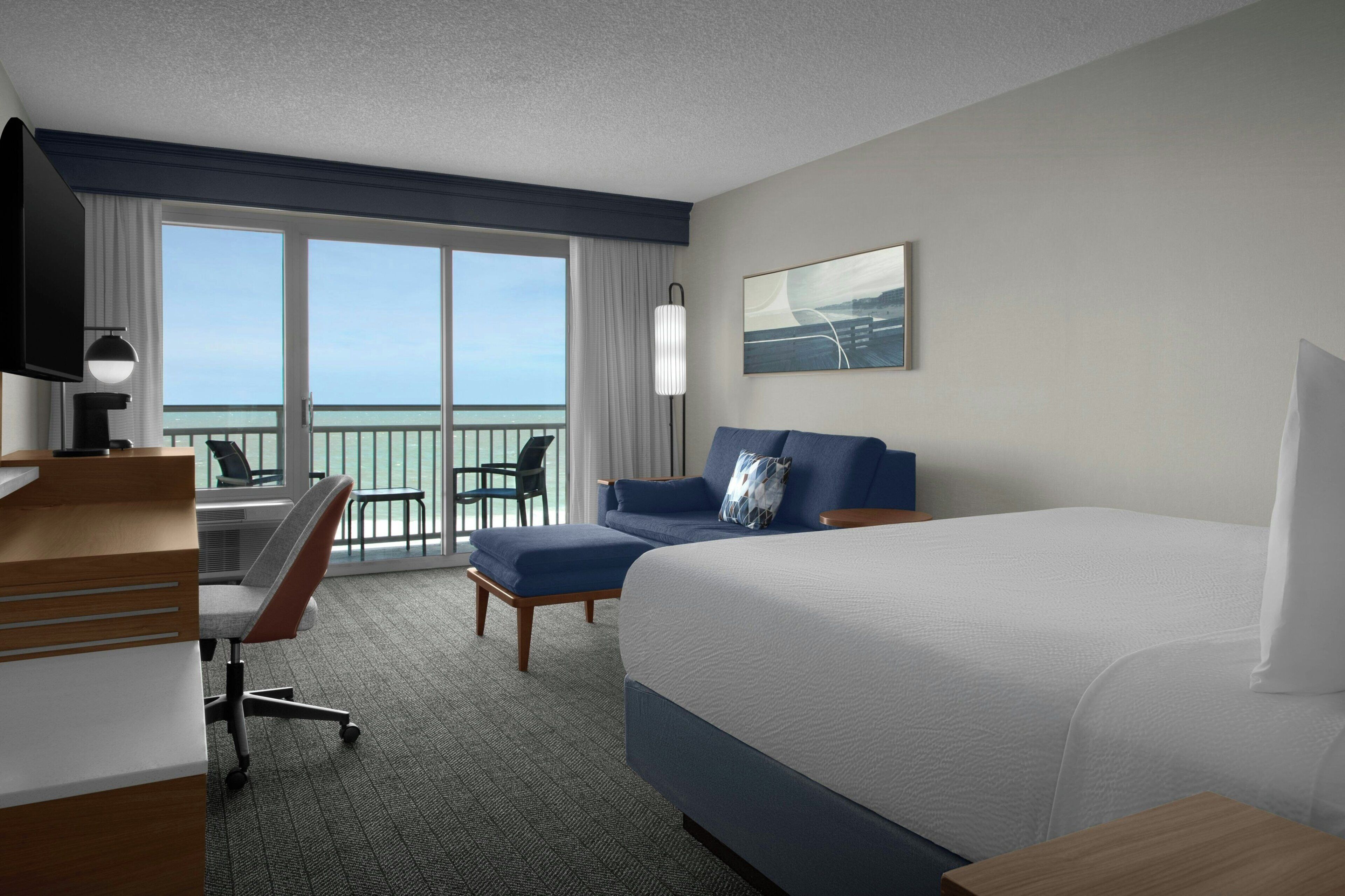 A hotel room with a bed, desk, chair, and a view of the ocean.