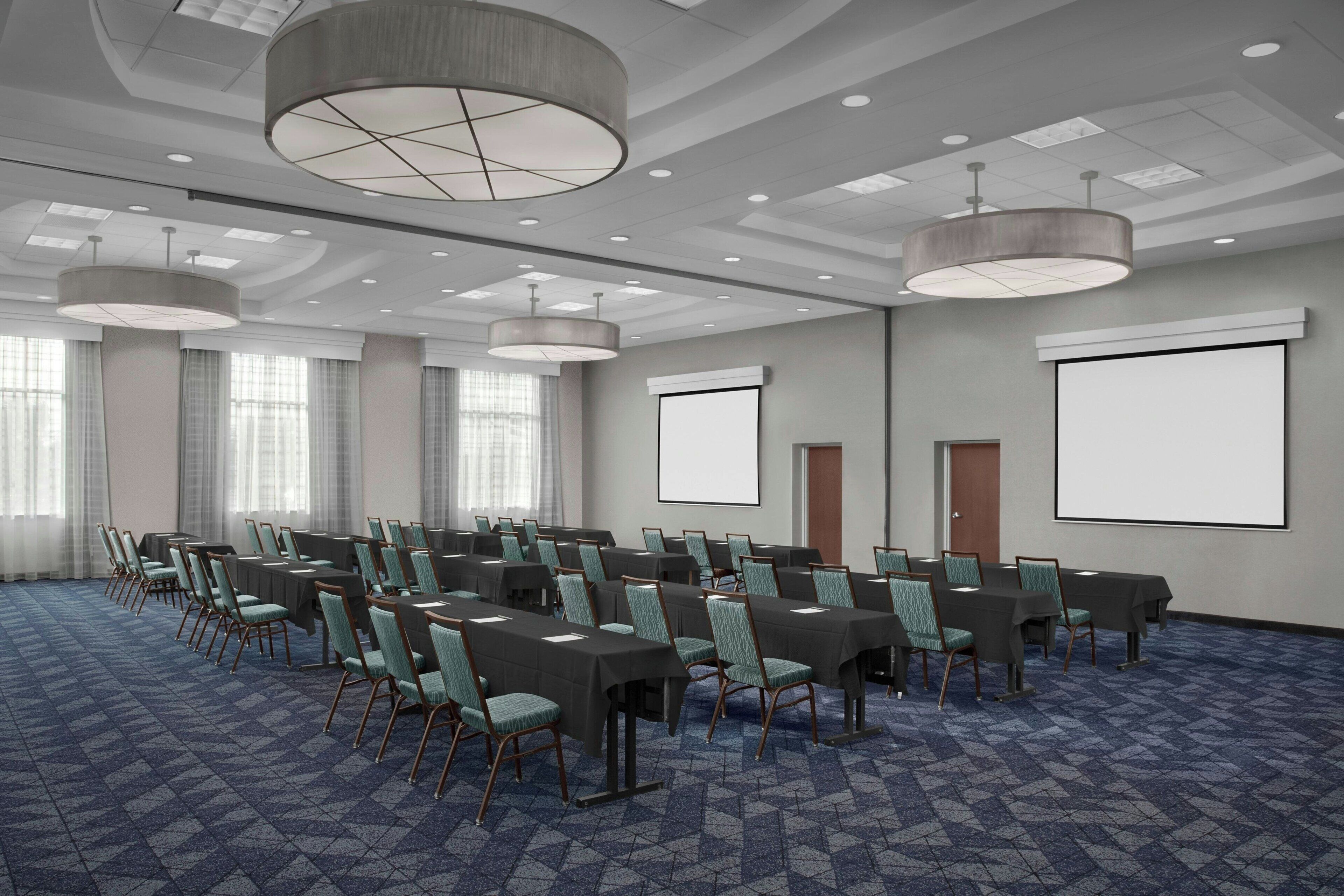 A conference room with a long table, chairs, a projector screen, and a carpeted floor.