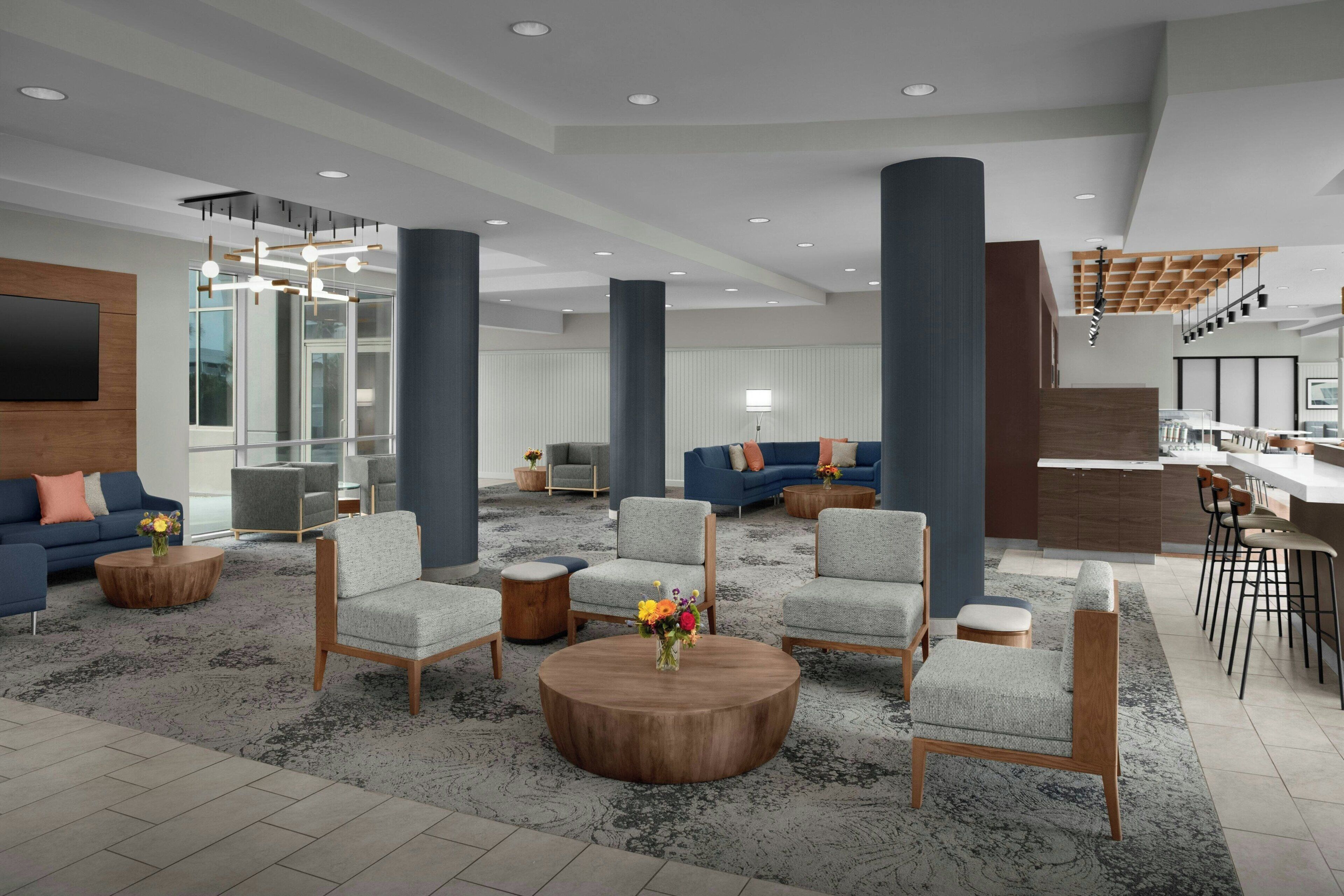 A spacious lobby with a modern design, featuring a mix of seating areas, a bar, and a staircase.