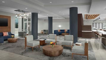 A spacious lobby with a modern design, featuring a mix of seating areas, a bar, and a staircase.