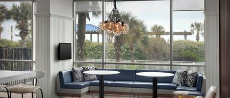 A modern interior with a sectional sofa, round tables, and a large window with a view of palm trees and a bridge.