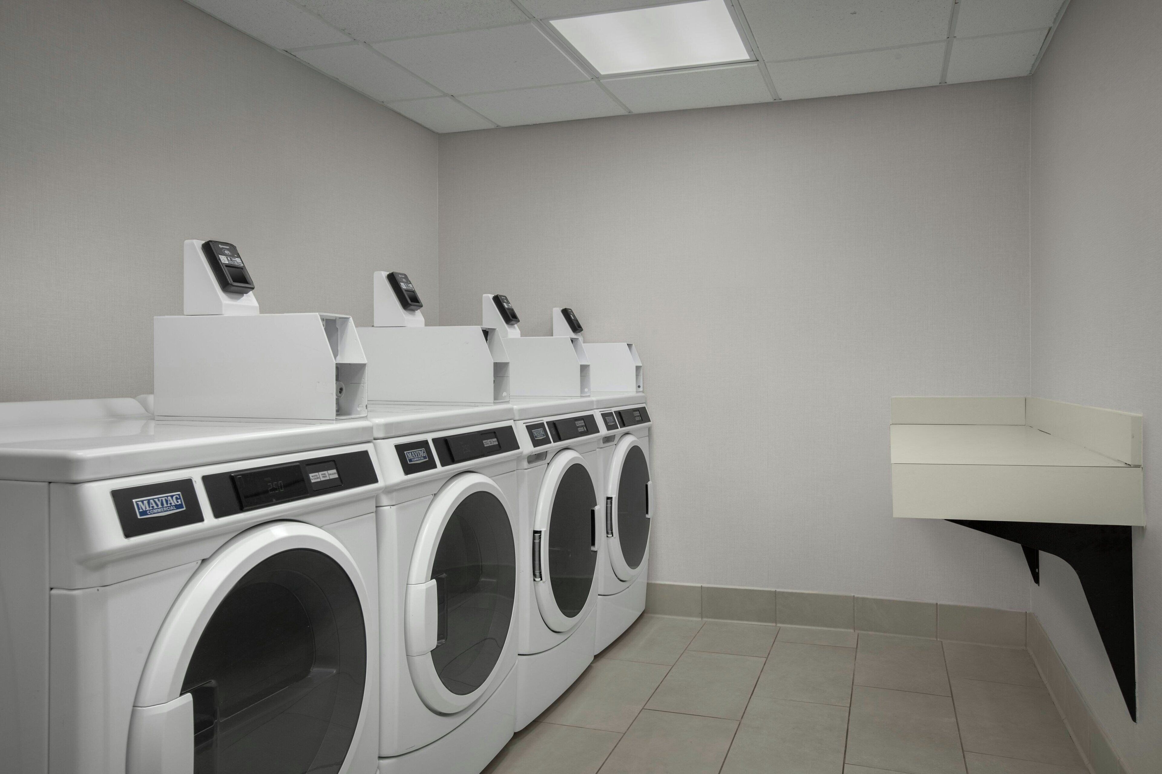 A laundry room with a row of white front-loading washers and dryers, a white sink, and a tiled floor.
