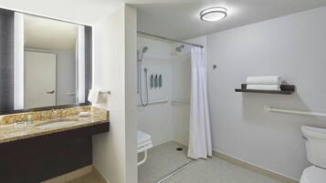 A modern bathroom with a granite countertop sink, a shower with a glass door, and a toilet with a grab bar.