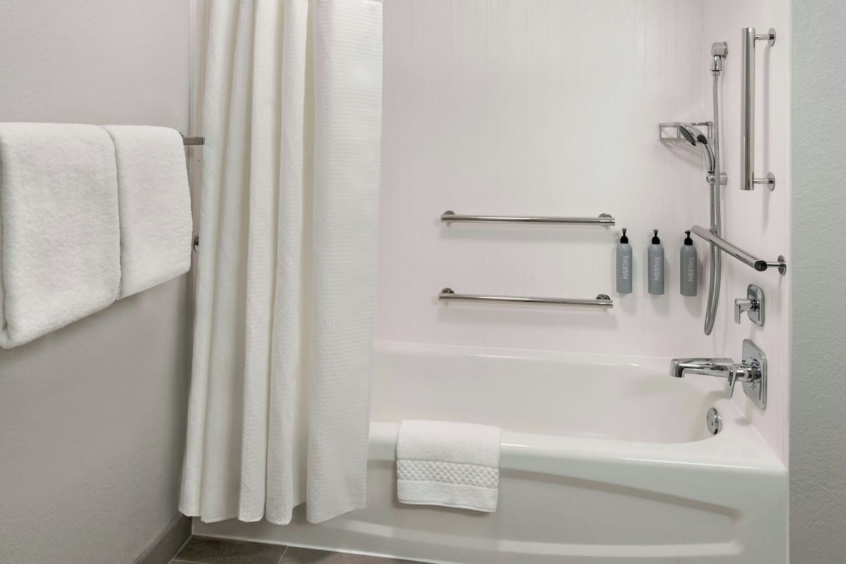 Une salle de bain moderne équipée d’une baignoire, d’une douche et de barres d’appui.