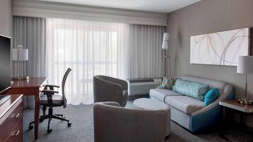 A hotel room with a desk, office chair, sofa, and a large window with curtains.