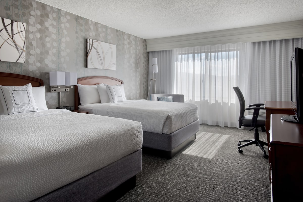 Une chambre d’hôtel avec deux lits, un bureau, une chaise et une lampe.