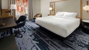 Une chambre d’hôtel avec un grand lit, un bureau avec une lampe, une chaise, un grand miroir et une fenêtre avec des rideaux.