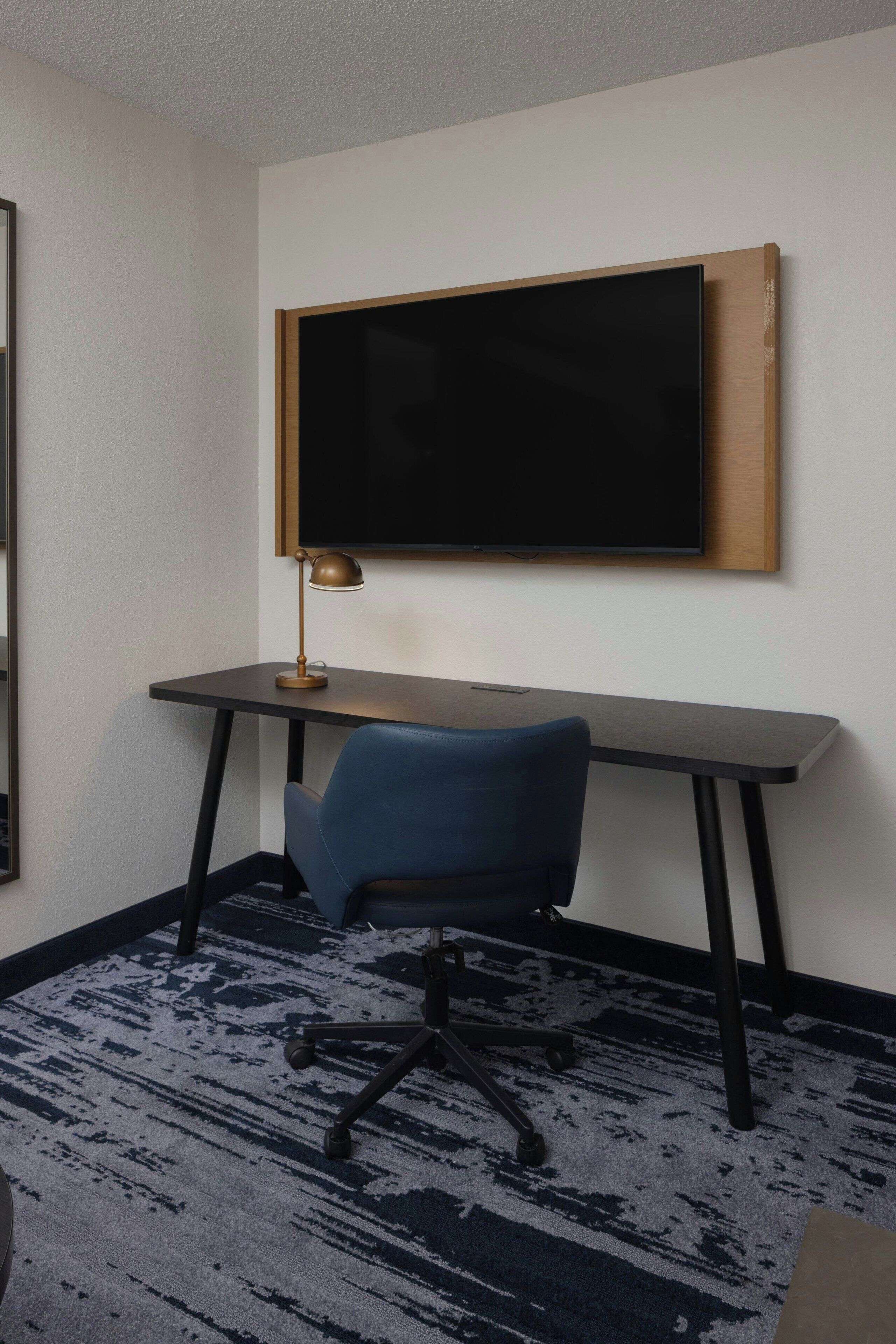 Un espace de bureau moderne comprenant un bureau, une chaise et un téléviseur à écran plat fixé au mur.