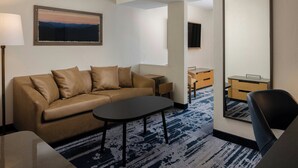 Une chambre d’hôtel moderne, équipée d’un canapé, d’une petite table, d’une chaise, d’un bureau et d’un grand miroir.