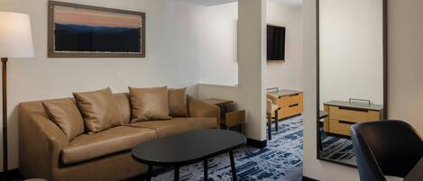 Een moderne hotelkamer met een sofa, een klein tafeltje, een stoel, een bureau en een grote spiegel.