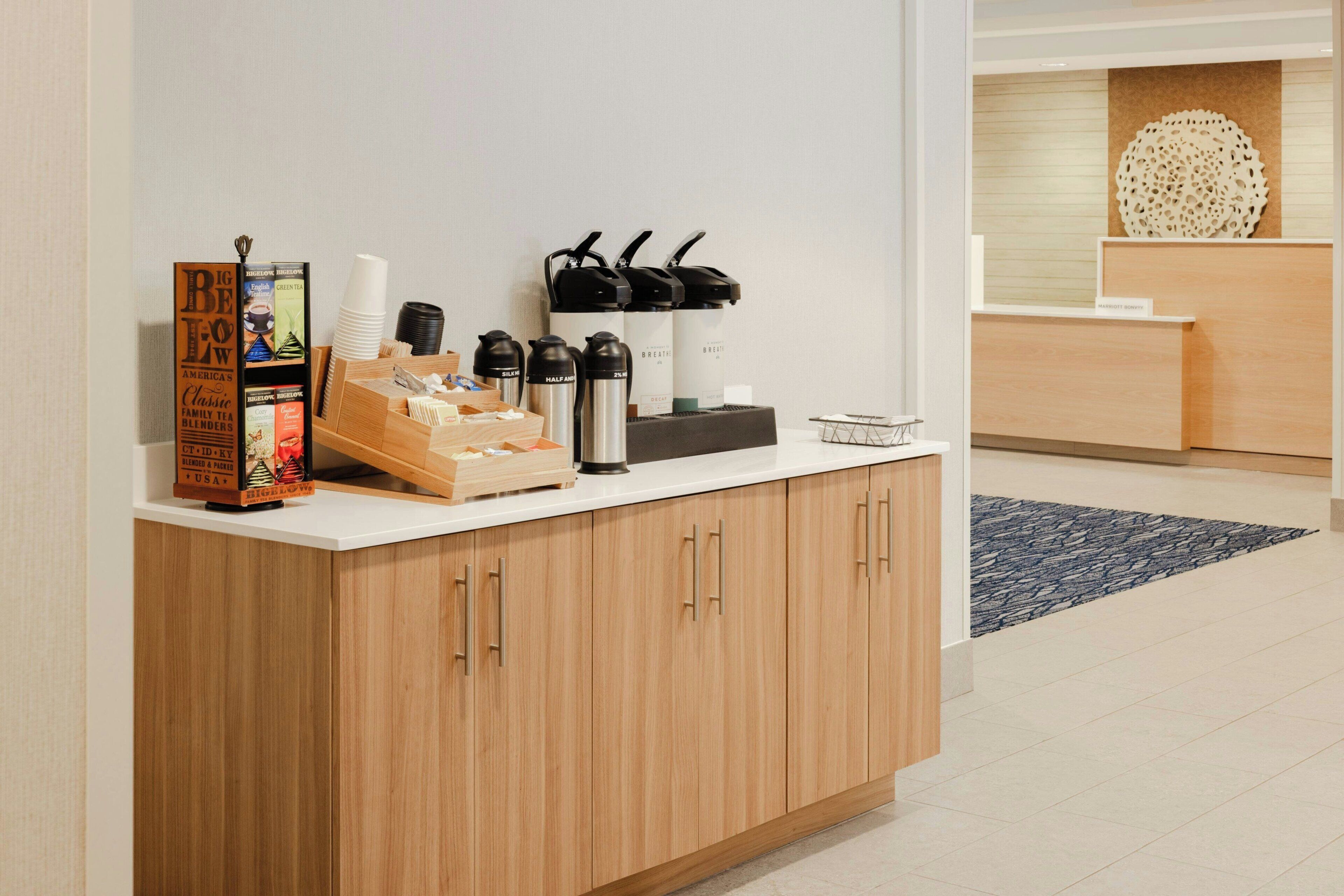Ein Hotel-Rezeptionsbereich mit einer Kaffeestation, einer Auswahl an Teesorten und einer Wanddekoration.