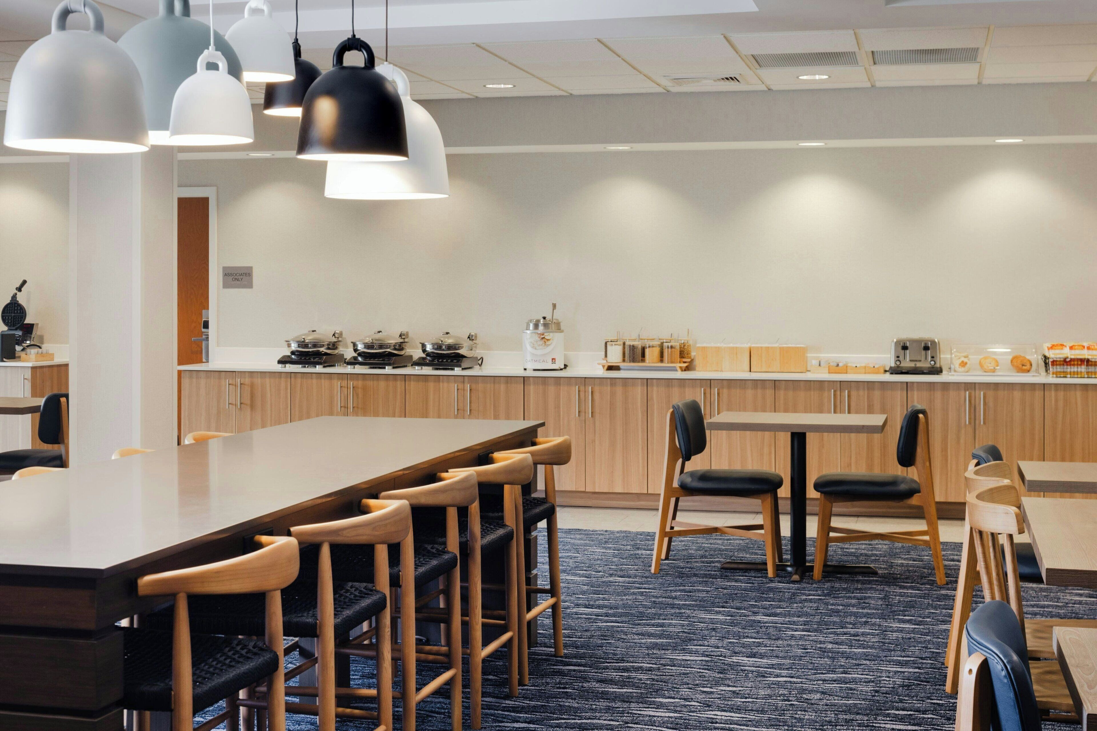 A modern kitchen with a long counter, multiple cooking stations, and a seating area with tables and chairs.
