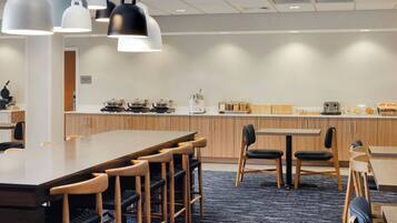 A modern kitchen with a long counter, multiple cooking stations, and a seating area with tables and chairs.