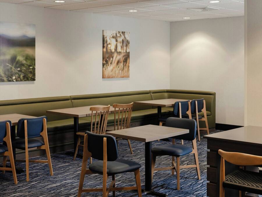 A hotel dining area with a green booth seating, wooden tables, and chairs.