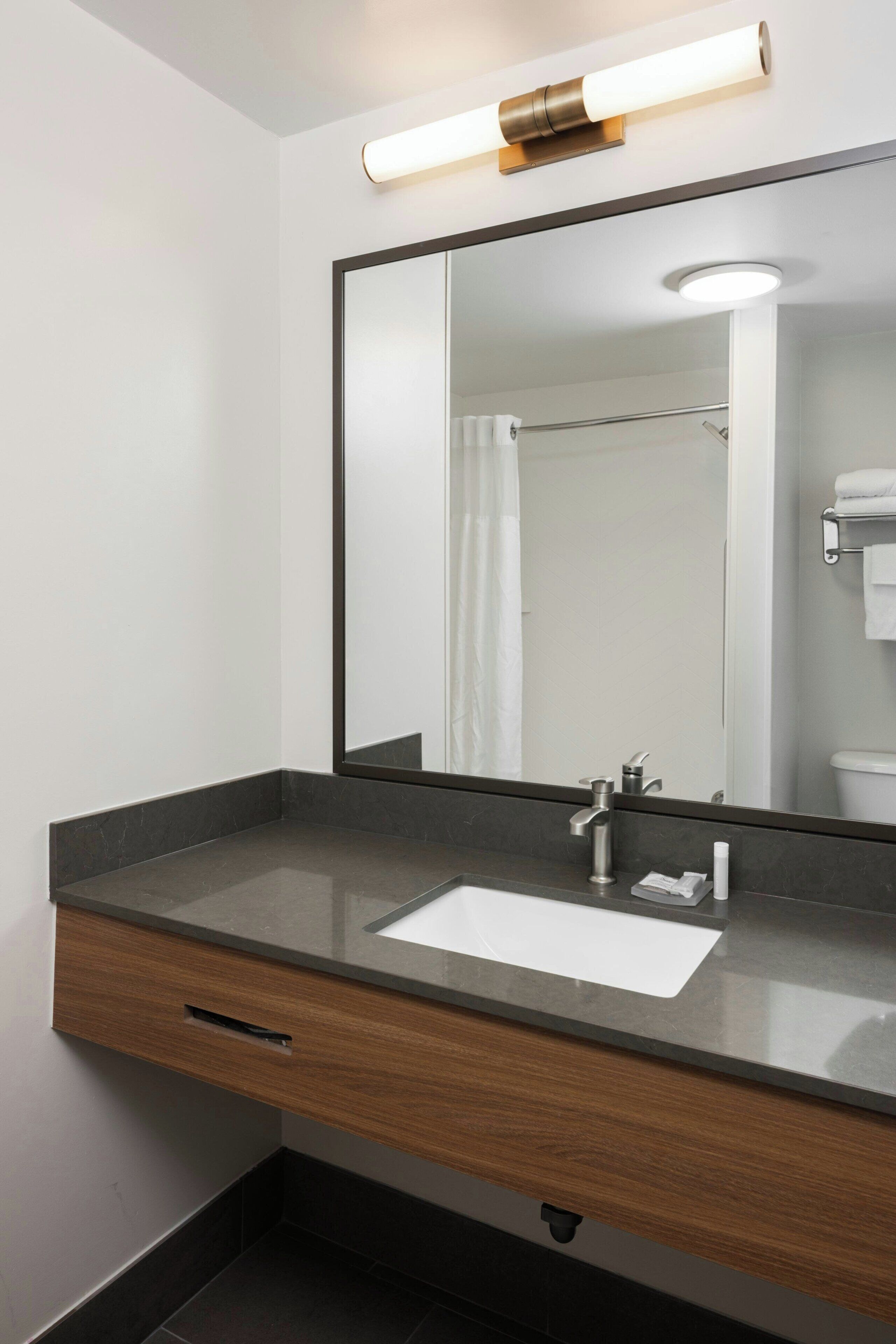 A modern bathroom with a large mirror, a sink, and a towel rack.